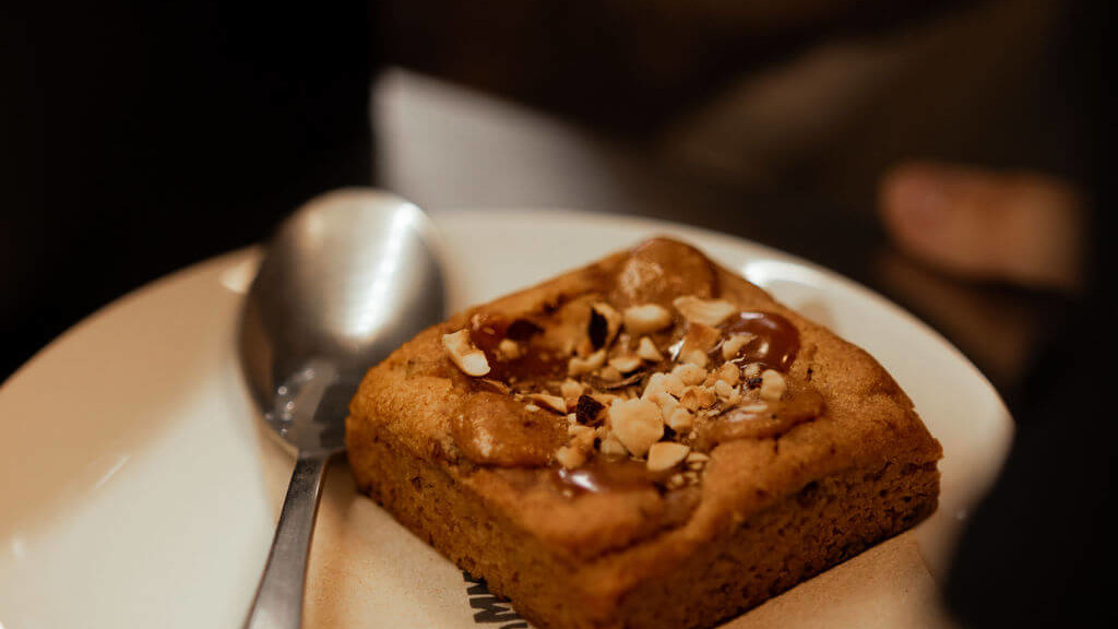 D&eacute;licieux brownie garni de caramel et d'&eacute;clats de noisettes, servi sur une assiette blanche avec une cuill&egrave;re au restaurant de La Commune &agrave; Lyon.