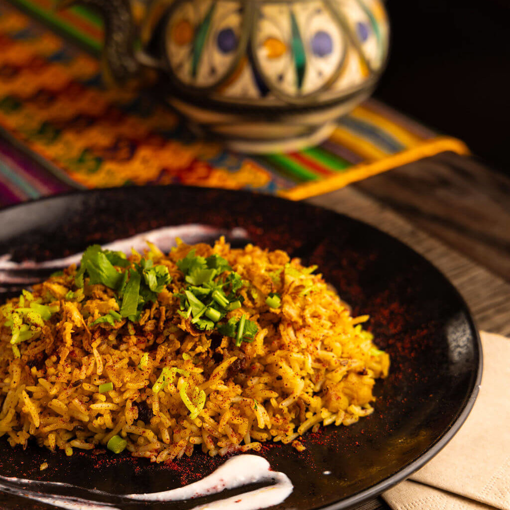 Riz épicé avec herbes fraîches et coriandre sur une assiette noire, inspiré des saveurs orientales, servi avec une théière décorative.