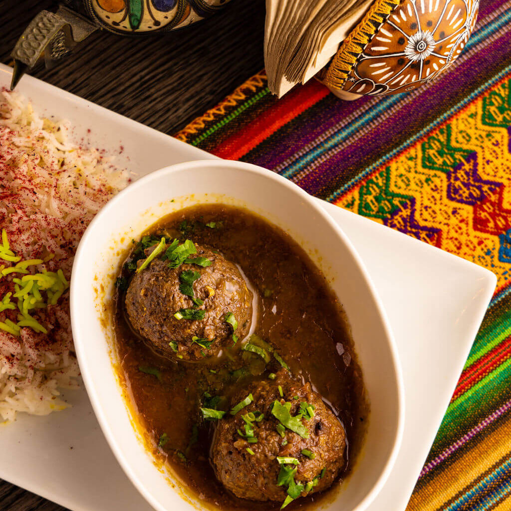 Plat de boulettes de viande dans une sauce épicée avec du riz parfumé, accompagné d’un service de table coloré et traditionnel.
