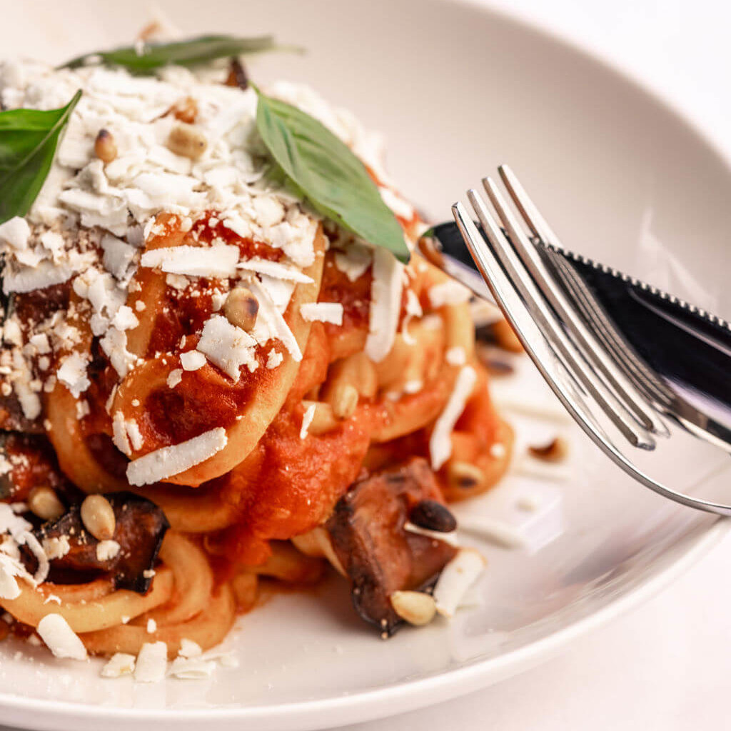 Assiette de pâtes napolitaines avec sauce tomate, garnies de basilic et de fromage râpé, servies dans un cadre lumineux et épuré.