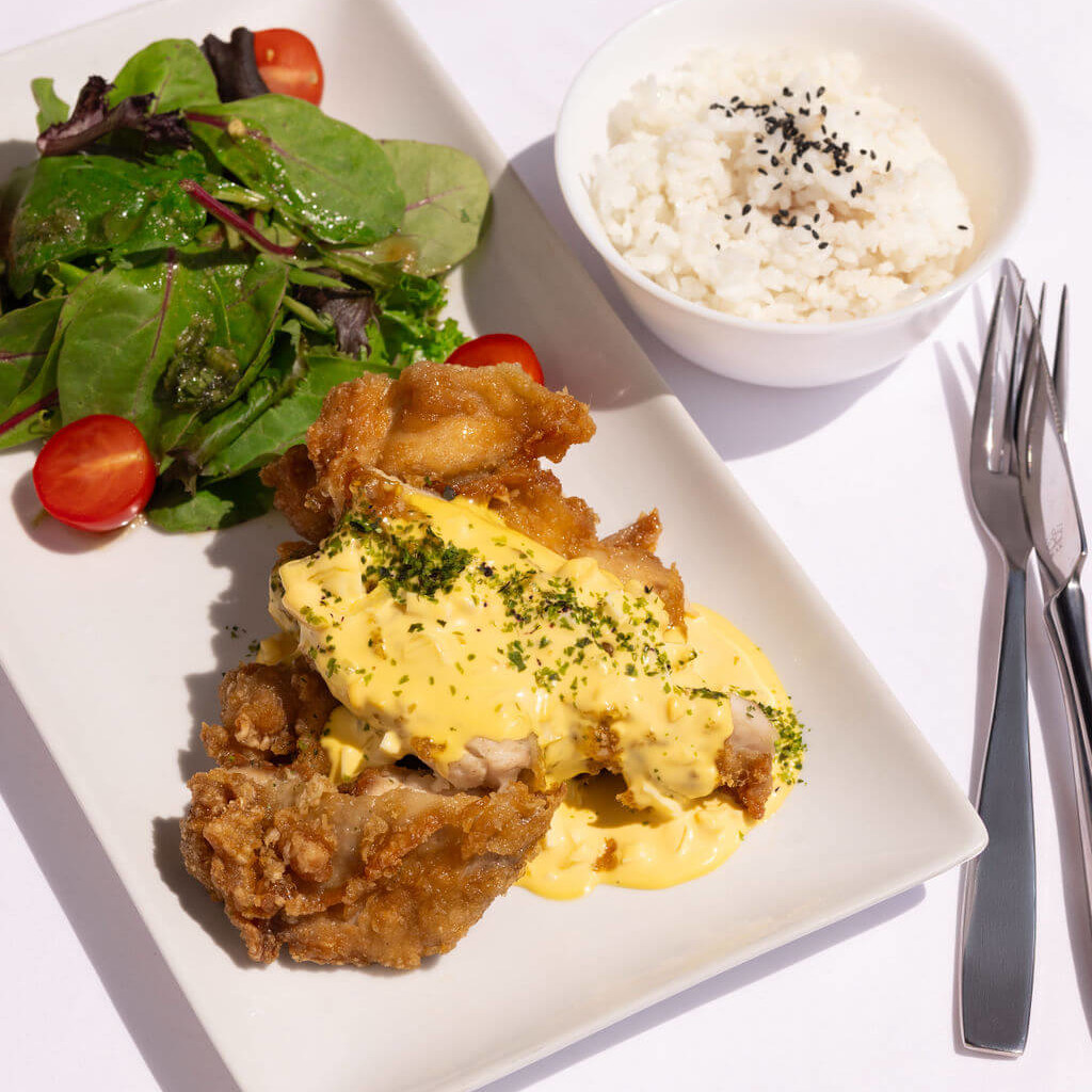 Poulet frit japonais avec une sauce crémeuse, accompagné de riz blanc et d'une salade verte sur une assiette moderne.