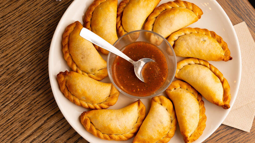 Assiette de d&eacute;licieux empanadas dor&eacute;s, accompagn&eacute;s d'une sauce salsa &eacute;pic&eacute;e, servie sur une table en bois au restaurant de La Commune, Lyon.