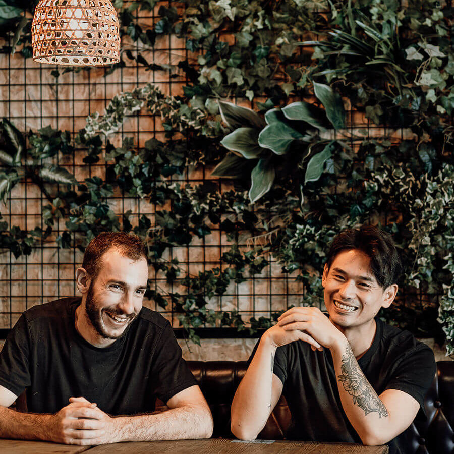 Deux chefs souriants posent devant un mur végétal, ambiance conviviale et détendue.