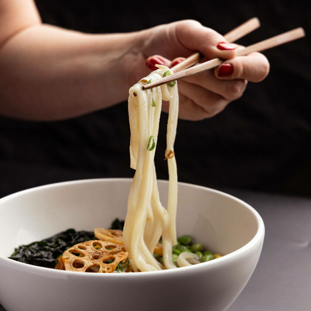 Gros plan sur des nouilles japonaises ramen, levées avec des baguettes en bois, mettant en valeur leur texture et leur fraîcheur.