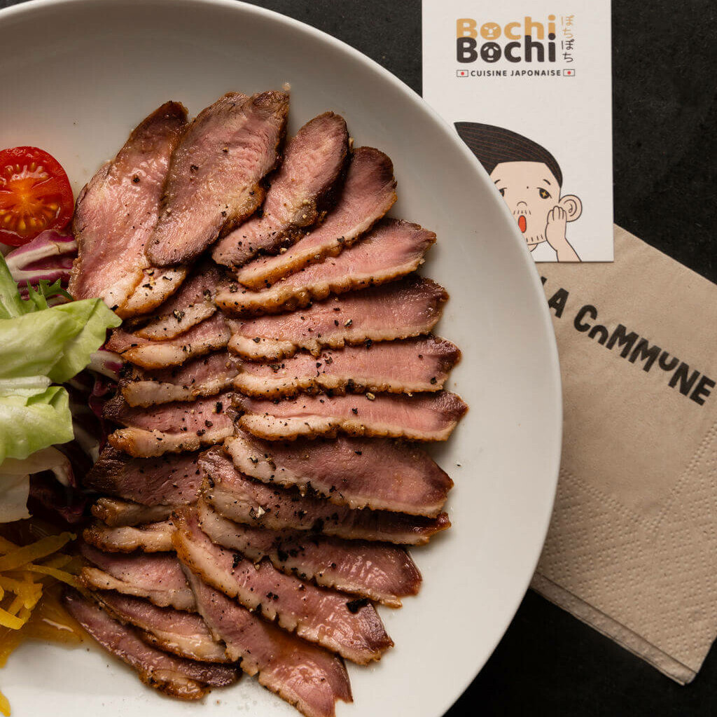 Assiette de magret de canard finement tranché, assaisonné de poivre, accompagné de salade, tomate cerise et pickles, servie chez Bochi Bochi, cuisine japonaise.