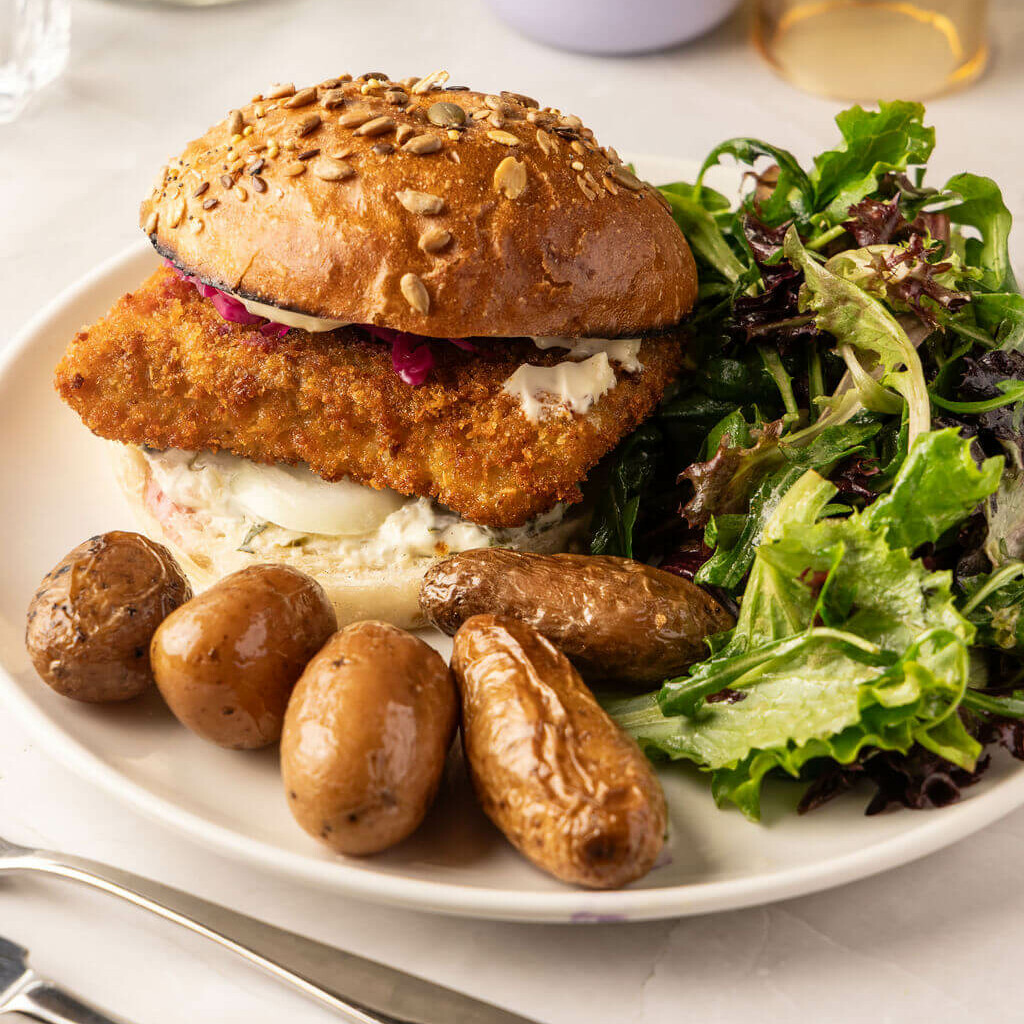 Burger croustillant au poisson pané, servi avec salade verte et pommes de terre – menu complet et équilibré.
