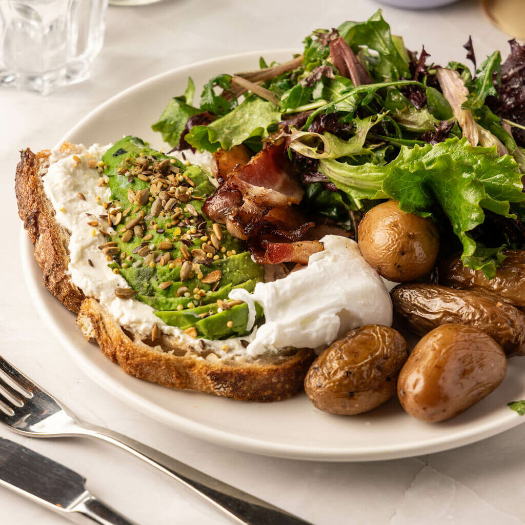 Avocado toast crémeux avec œuf poché, bacon grillé, graines et salade – petit-déjeuner sain et gourmand.