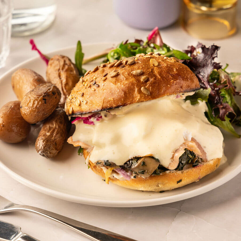 Burger fondant au fromage, champignons et légumes, accompagné de salade et pommes de terre rôties – plat réconfortant.
