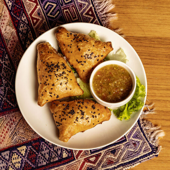 Trio de samossas afghans dorés au four, garnis de légumes ou viande, servis avec sauce maison sur lit de salade.