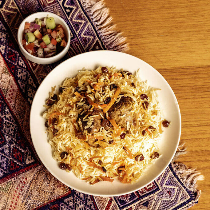 Kabuli Palaw, plat afghan emblématique : riz basmati, carottes, raisins secs et viande, accompagné d’une salade fraîche.