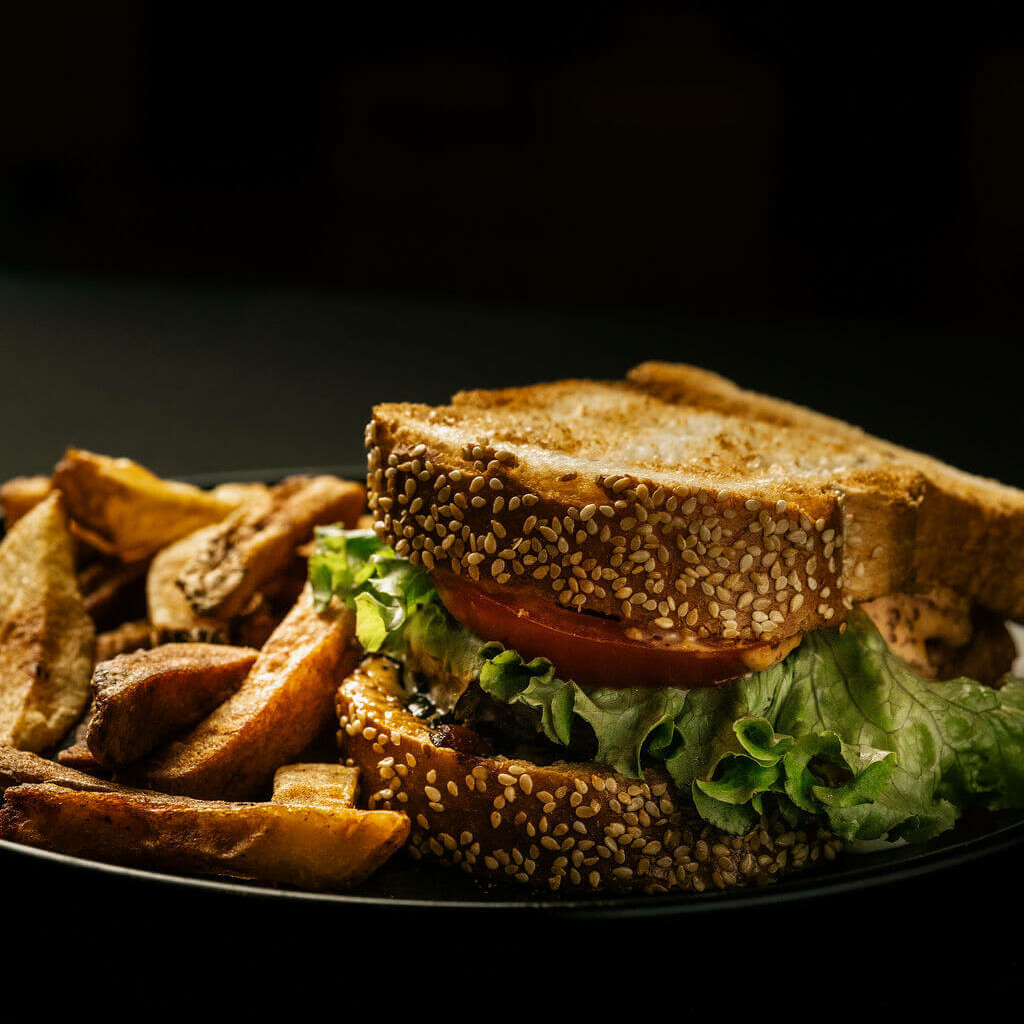 Burger au pain de mie aux graines de sésame, garni de tomate et salade, servi avec frites maison.