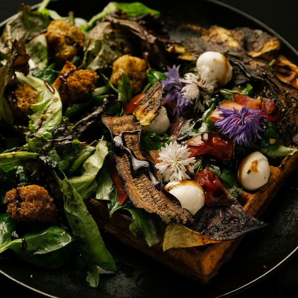 Gaufre salée garnie de légumes grillés, mozzarella, fleurs comestibles et salade verte.