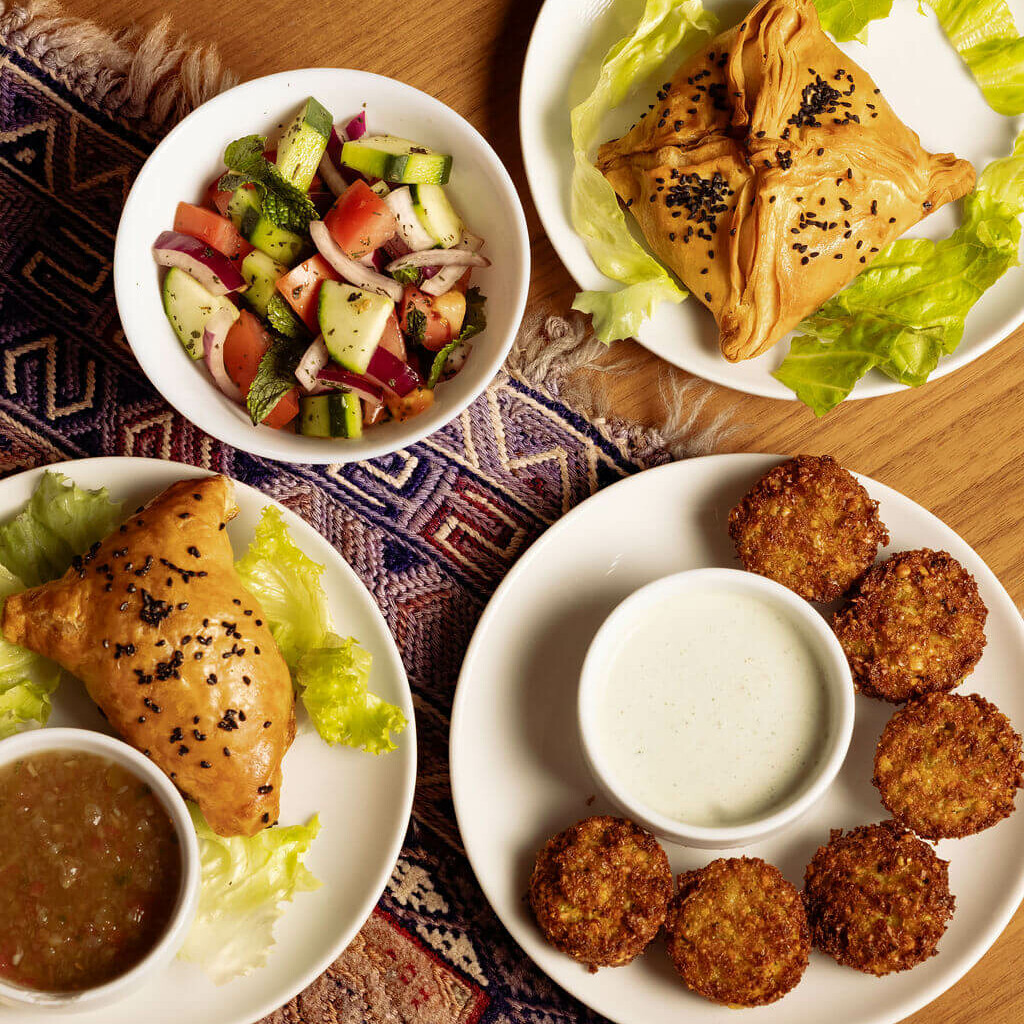 Assortiment d’entrées afghanes : samossas, falafels et salade fraîche, servis avec sauces, sur fond de tapis traditionnel.