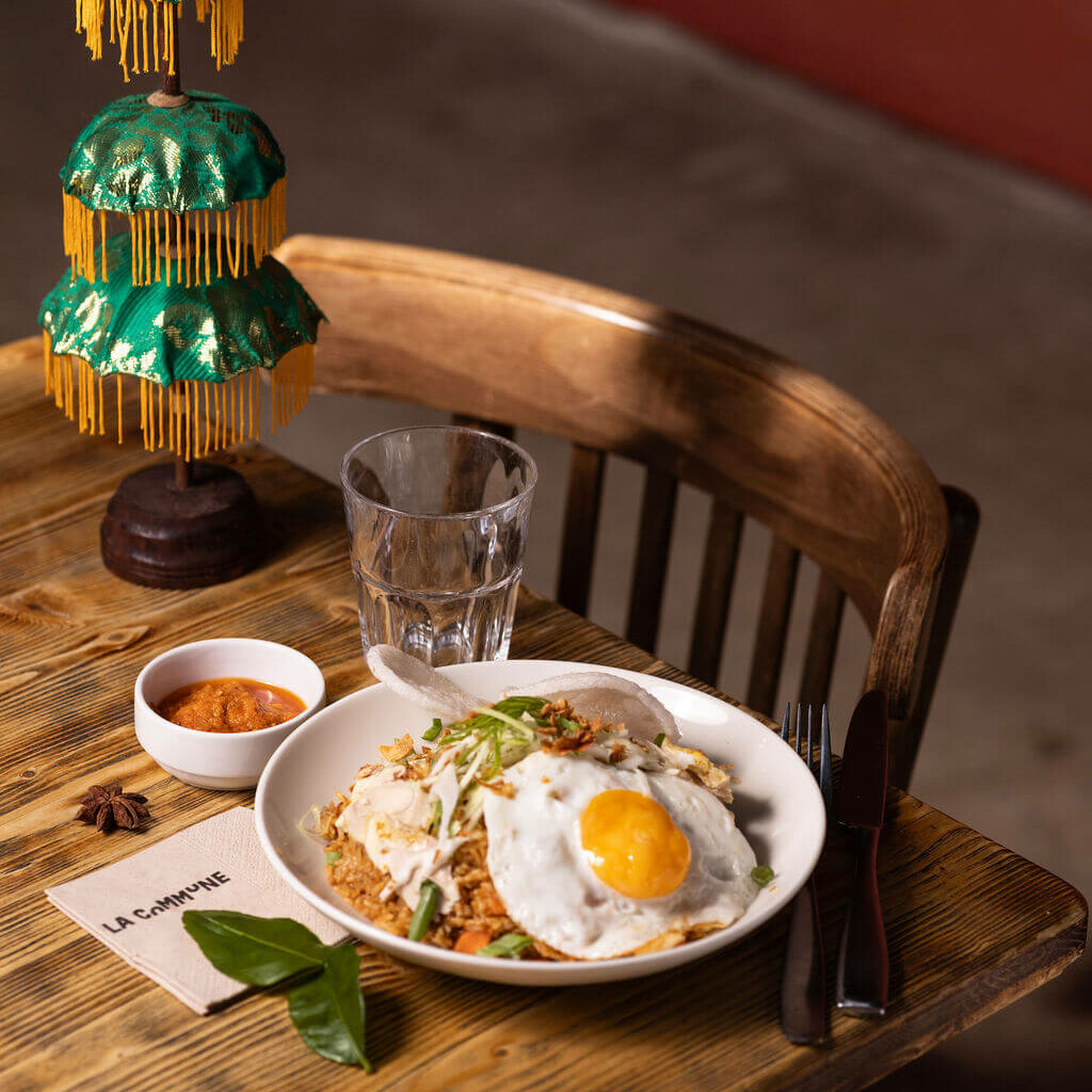 Assiette de nasi goreng indonésien avec œuf au plat, sambal et condiments, servie sur une table en bois.