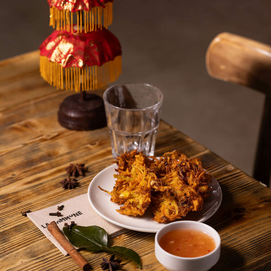 Assiette de beignets indonésiens frits servis avec une sauce, sur une table en bois décorée d’épices et d’un petit parasol traditionnel.