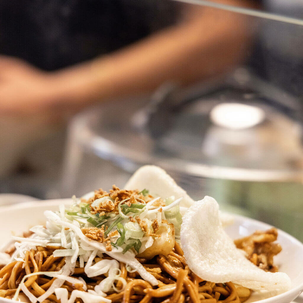 Assiette de nouilles indonésiennes Java Rempah garnies de légumes, oignons frits et chips de crevette, photographiée en gros plan.