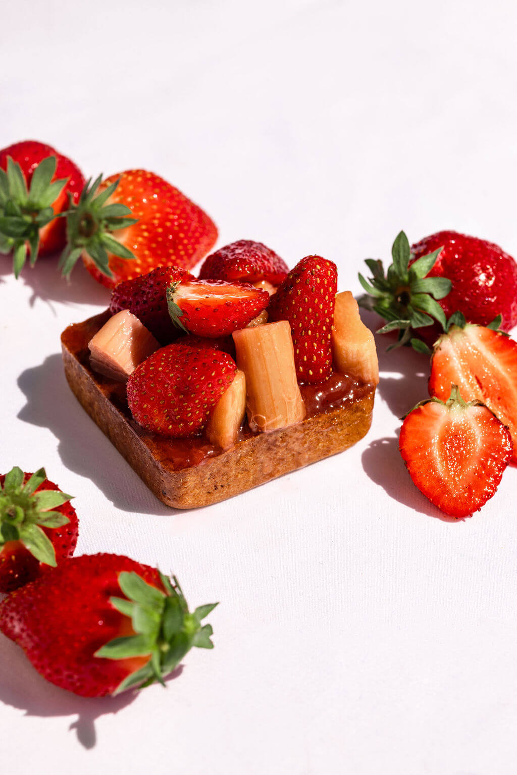 Tartelette garnie de fraises et de rhubarbe, accompagnée de fraises fraîches. Un dessert fruité et rafraîchissant pour les amateurs de saveurs naturelles.