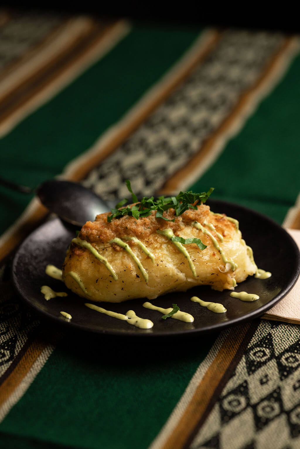 Pomme de terre farcie au poulet et herbes, nappée de sauce verte sur une assiette noire, un incontournable de la cuisine andine.