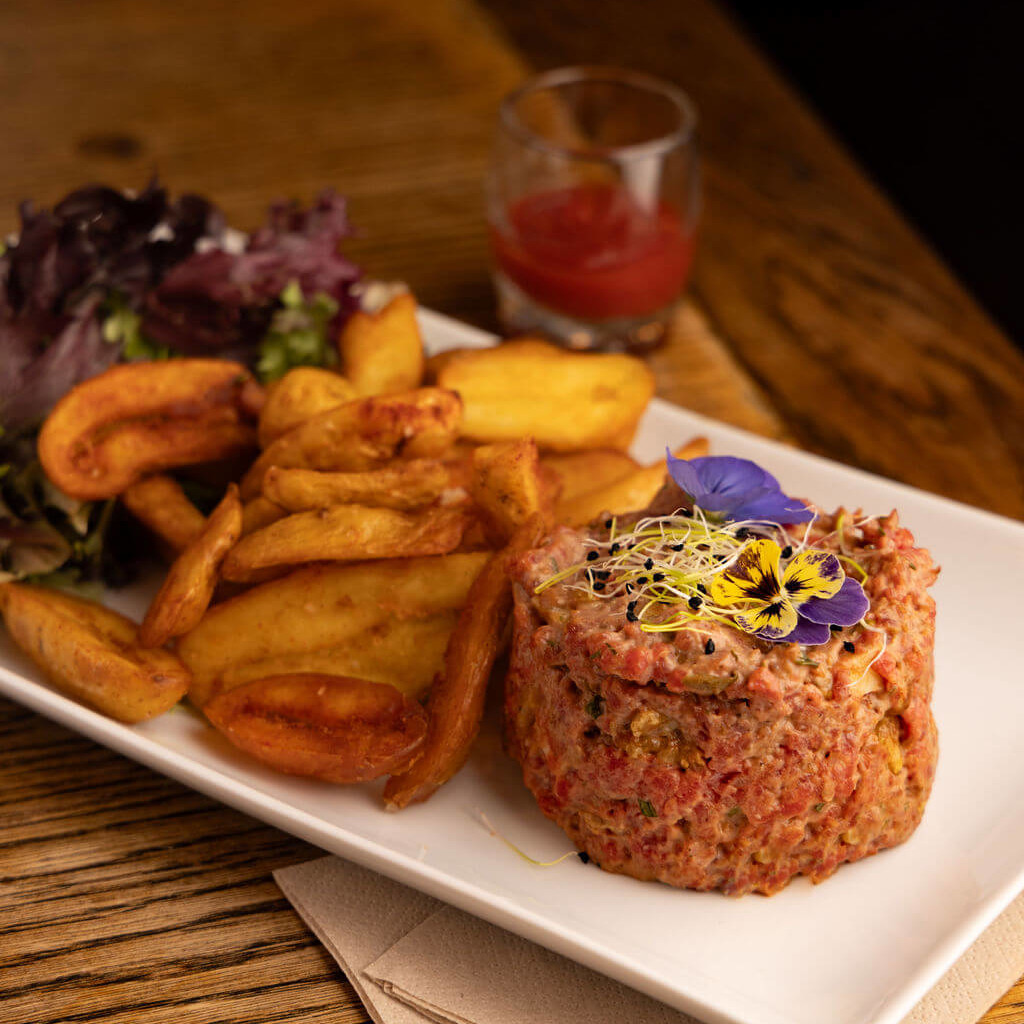 Tartare de viande fraîche avec pommes de terre croustillantes et salade verte.