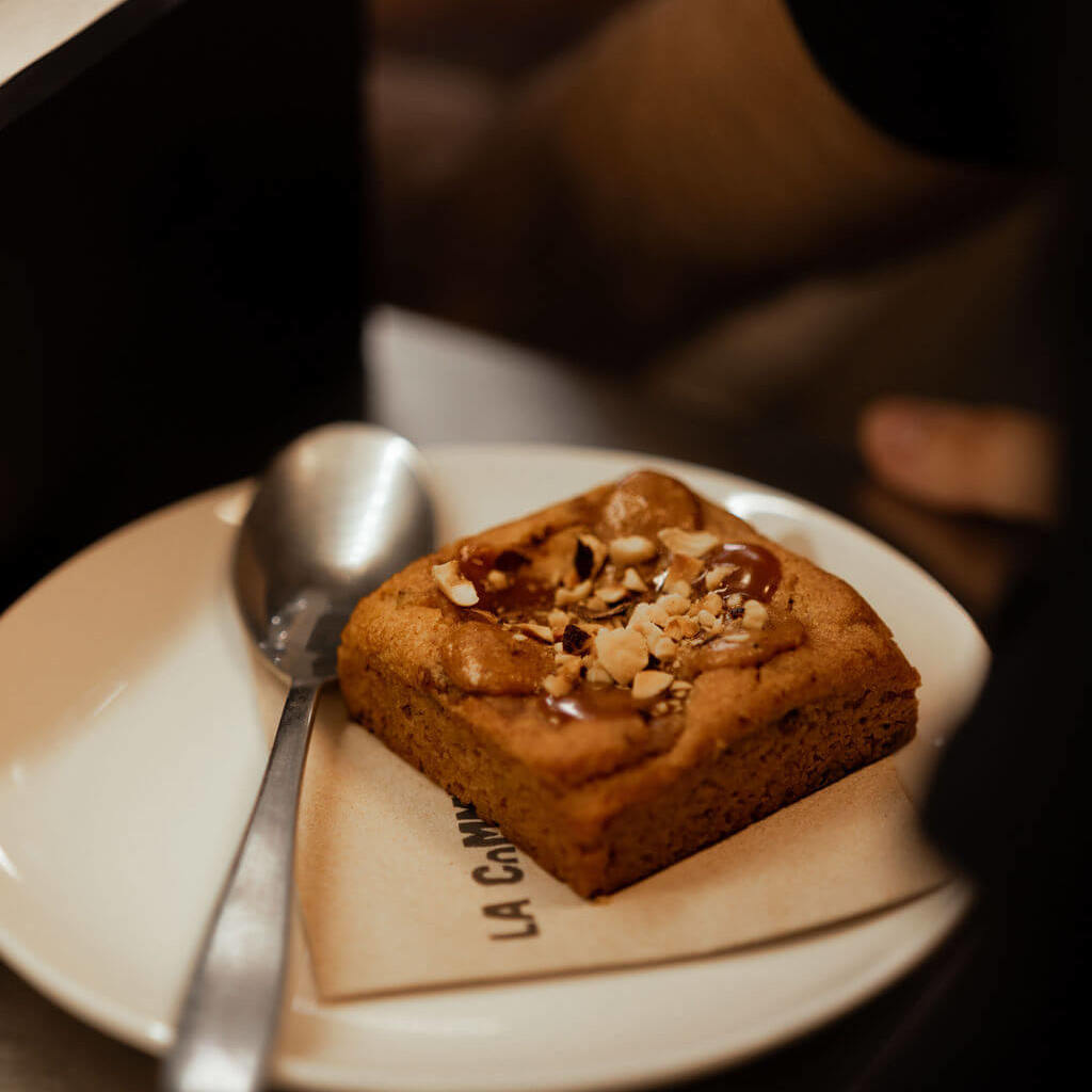 Délicieux brownie garni de caramel et d'éclats de noisettes, servi sur une assiette blanche avec une cuillère au restaurant de La Commune à Lyon.