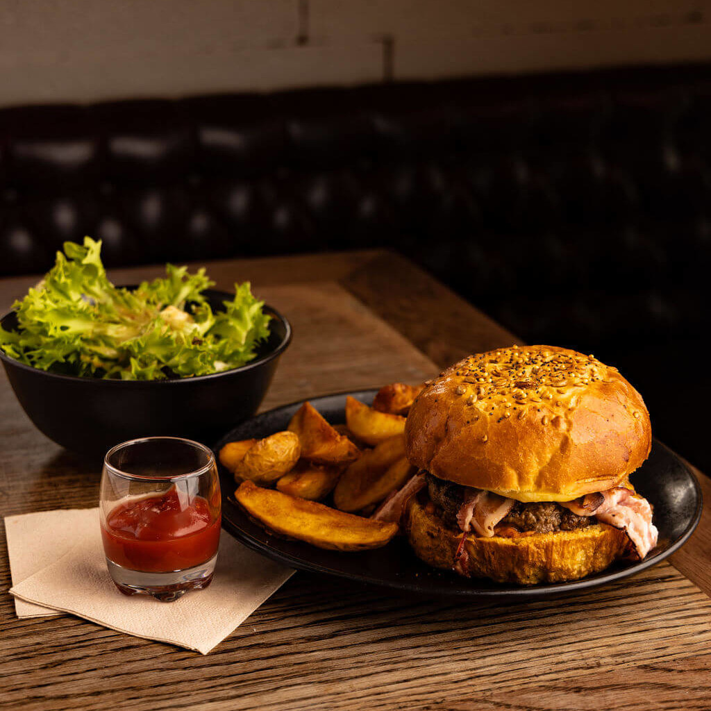 Burger gourmand avec steak de bœuf, bacon, frites maison et accompagnement de salade fraîche.