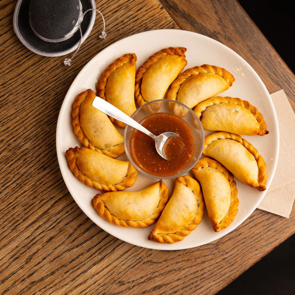 Assiette d'empanadas dorées servies avec une sauce épicée, spécialité de street food idéale pour un apéritif convivial.