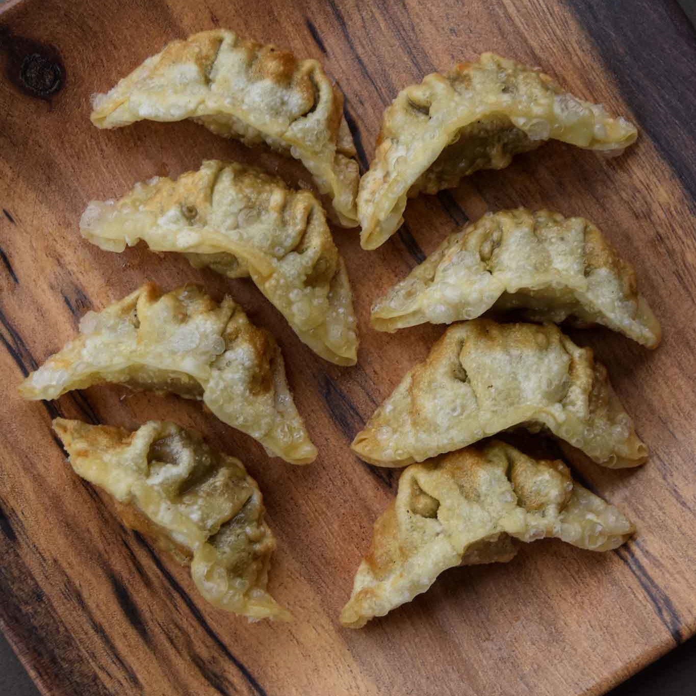 Gyozas frits dorés, disposés sur un plateau en bois, parfaits pour une entrée ou un accompagnement asiatique.