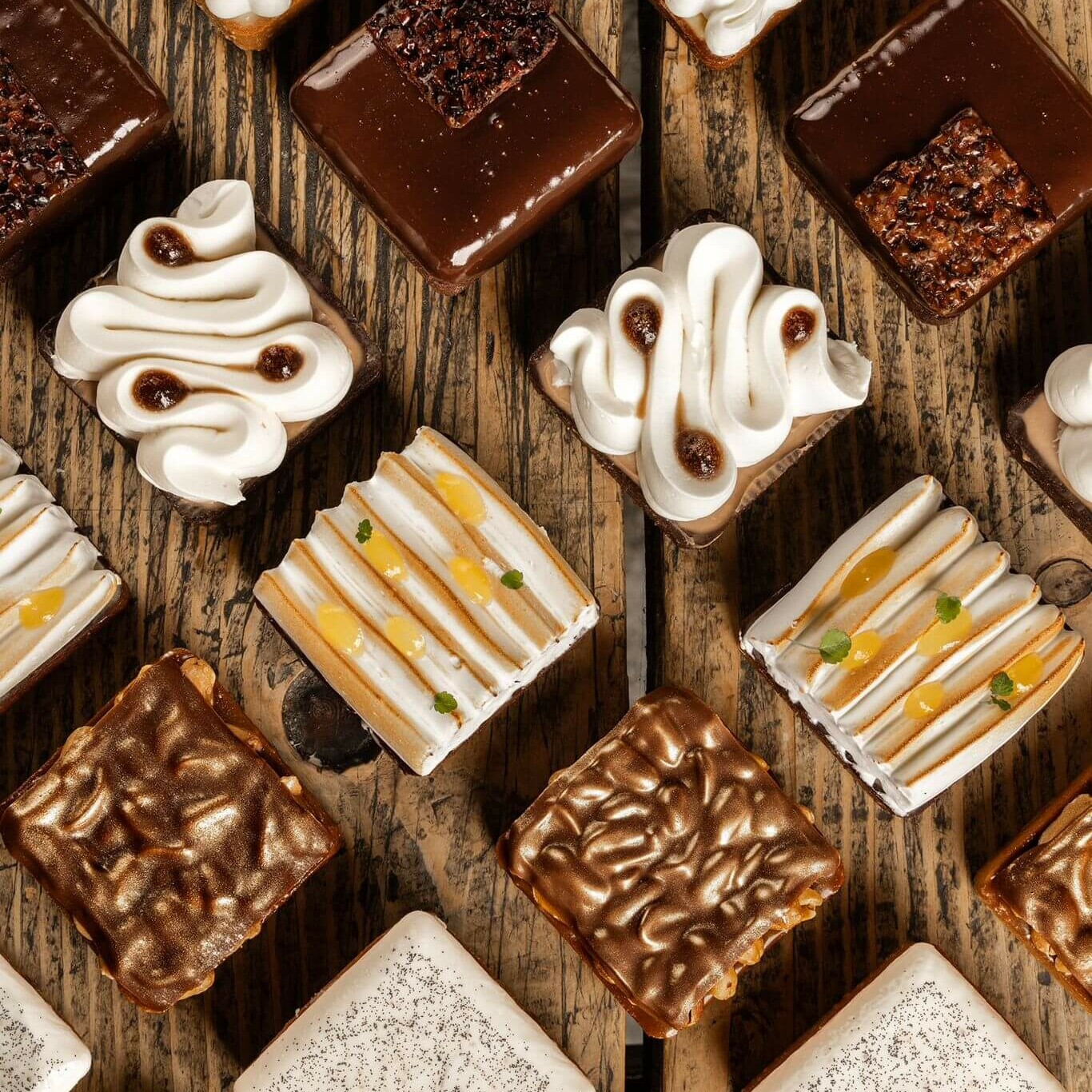 Assortiment de pâtisseries carrées gourmandes aux garnitures variées, présenté sur un fond en bois rustique.