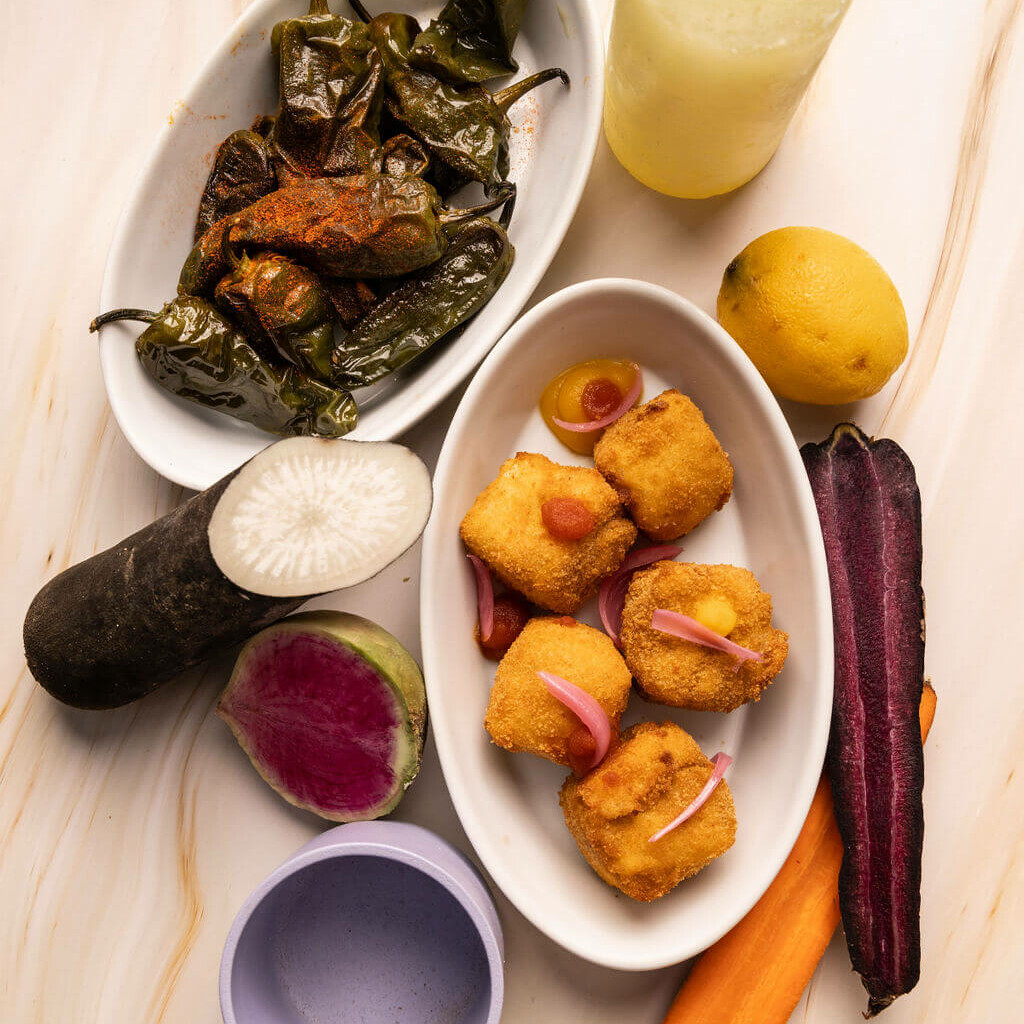 Assortiment de tapas avec légumes rôtis, croquettes panées et sauces colorées sur une table en marbre.