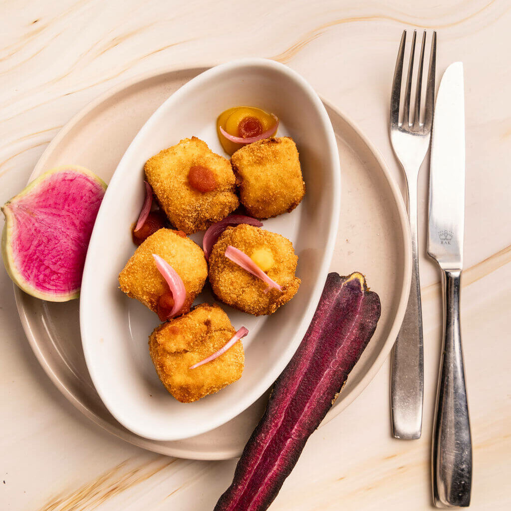 Croquettes panées croustillantes accompagnées de légumes colorés, servies dans un plat blanc.