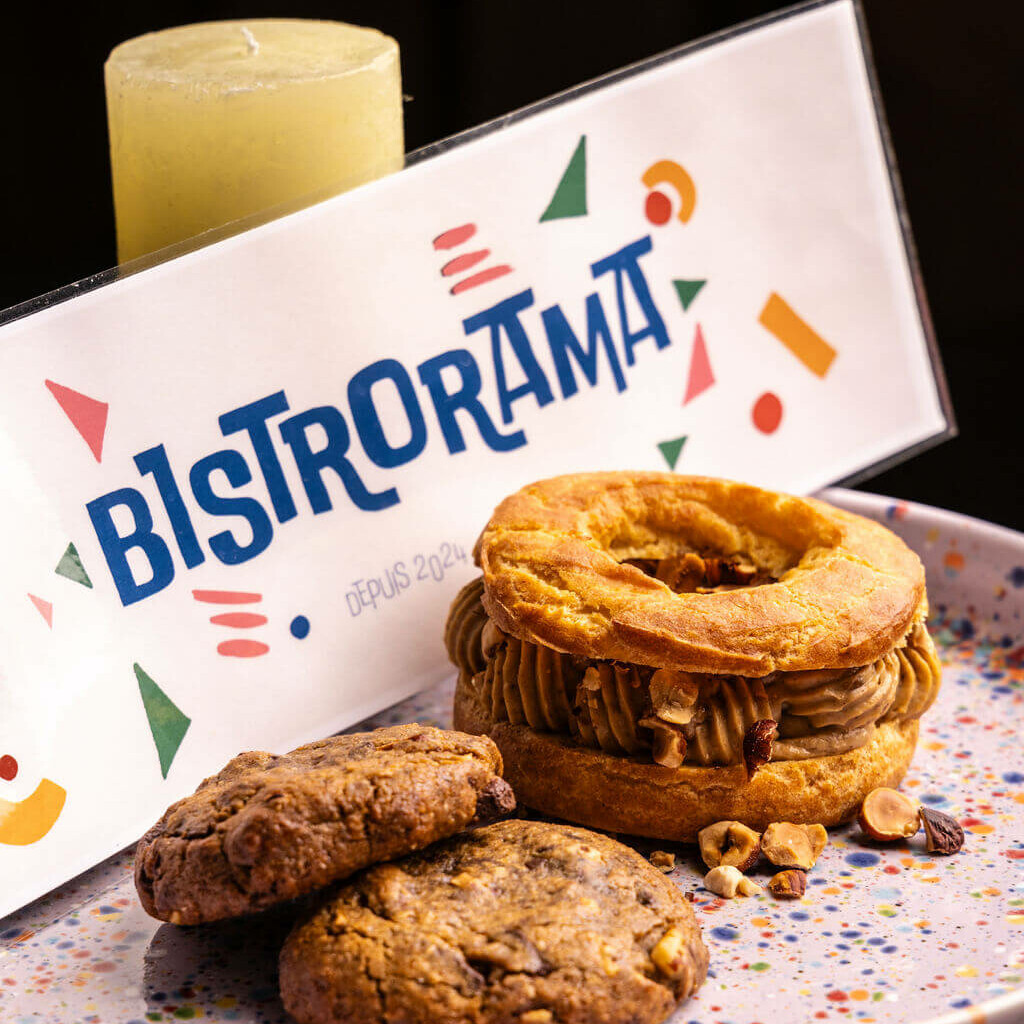 Assiette de desserts avec un Paris-Brest et des cookies au chocolat, devant une enseigne Bistrorama.